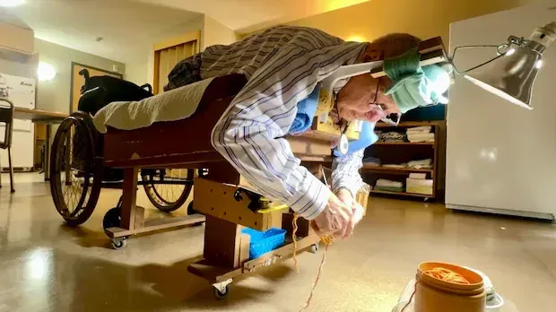 Man who lost legs to MS warming heads and hearts by knitting tuques on custom-made cot